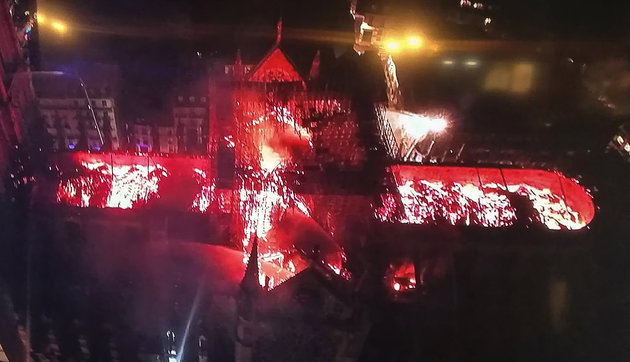 An image taken from a television screen shows an aerial view of the Notre-Dame Cathedral engulfed in flames on April 15, 2019, in the French capital Paris. - A huge fire swept through the roof of the famed Notre-Dame Cathedral in central Paris on April 15, 2019, sending flames and huge clouds of grey smoke billowing into the sky. The flames and smoke plumed from the spire and roof of the gothic cathedral, visited by millions of people a year. A spokesman for the cathedral told AFP that the wooden structure supporting the roof was being gutted by the blaze. (Photo by - / AFP)